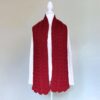 Red cable-knit scarf displayed on a white mannequin in front of a plain background. The scarf is thick, adding a cozy and elegant touch.