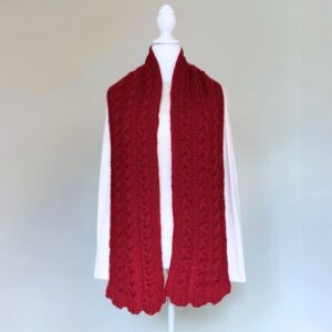 Red cable-knit scarf displayed on a white mannequin in front of a plain background. The scarf is thick, adding a cozy and elegant touch.