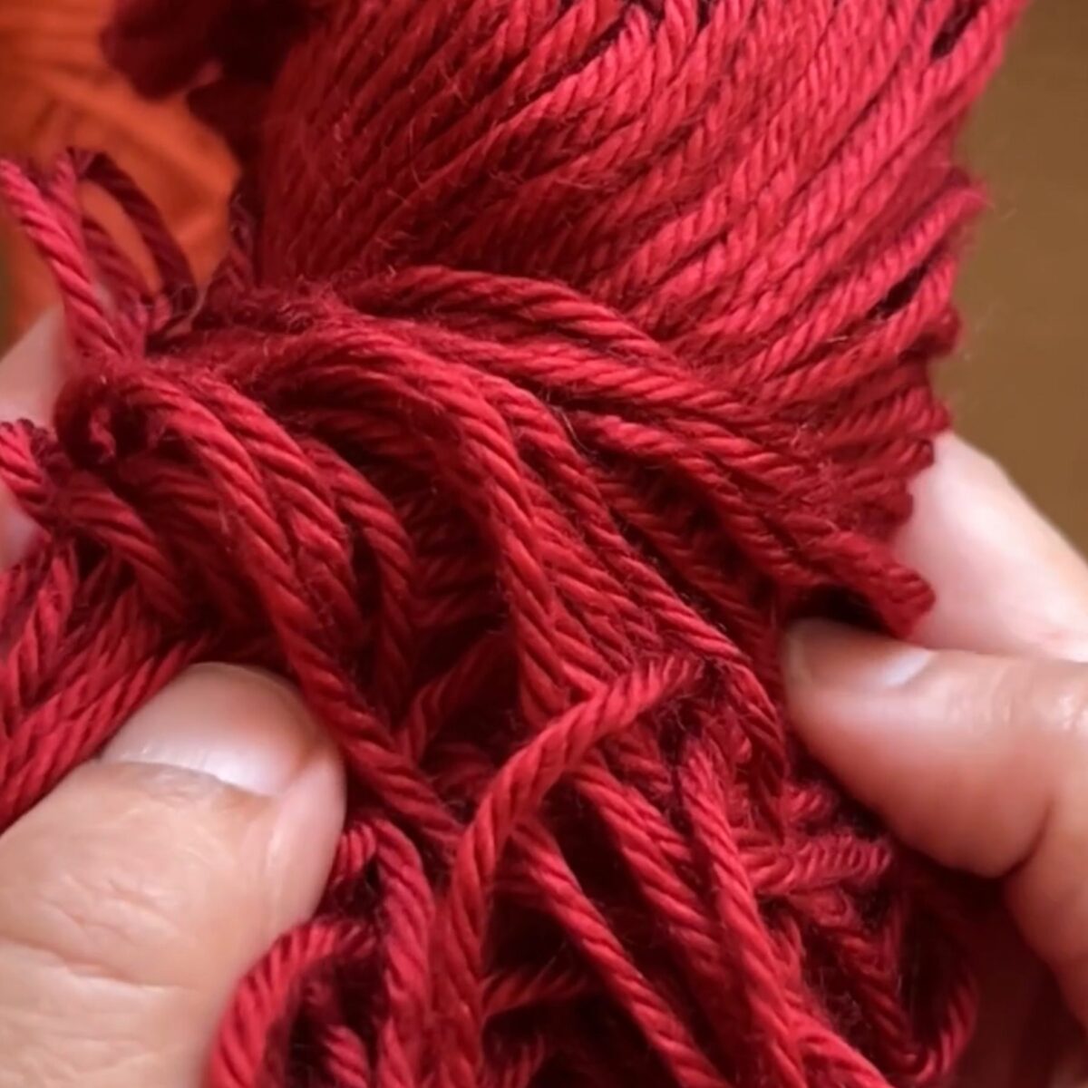 Close-up of hands holding a skein of deep red yarn