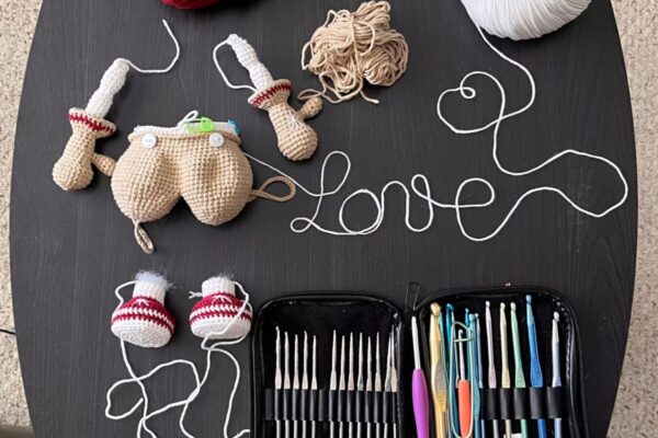 Ruth's crochet workspace — yarn, hooks, and an in-progress amigurumi arranged with yarn spelling 'love'