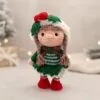 Crochet doll in festive attire with a green dress, red boots, and holly on a hat. Soft lighting and a blurred background create a cozy feel.