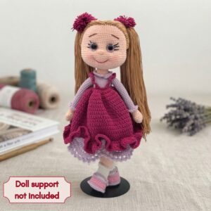 Crocheted doll with long brown hair and a pink dress stands on a black stand