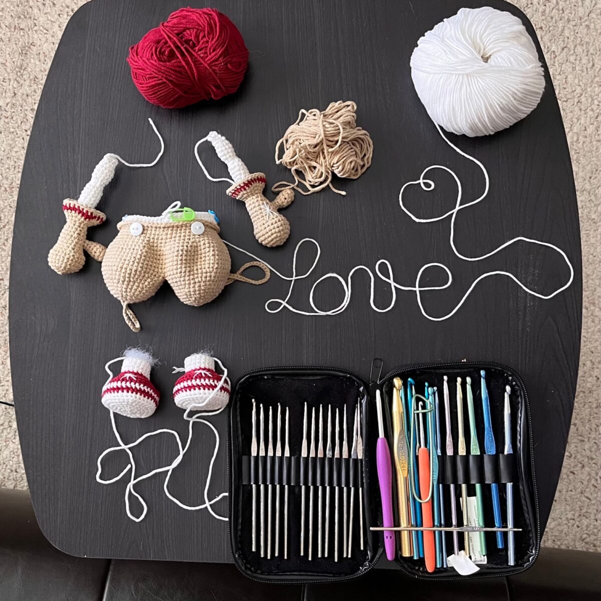 Ruth's crochet workspace — yarn, hooks, and an in-progress amigurumi arranged with yarn spelling 'love'